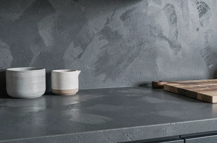 Plan de travail et crédence en béton ciré teinté dans la masse de couleur gris ardoise, avec texture lisse et variations tonales subtiles dans une cuisine contemporaine.