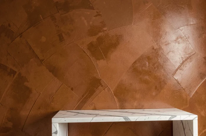 Mur d'une salle à manger recouvert d'enduit à la chaux pigmenté en terre de Sienne appliqué en stuc ferré, révélant une surface lustrée avec des reflets soyeux caractéristiques.