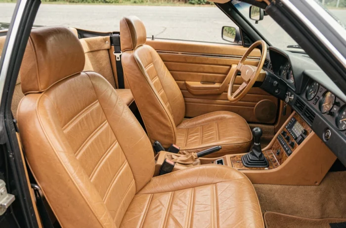 Intérieur authentique d'une Peugeot 305 cabriolet avec sièges en cuir caramel, tableau de bord analogique et volant à logo lion Peugeot