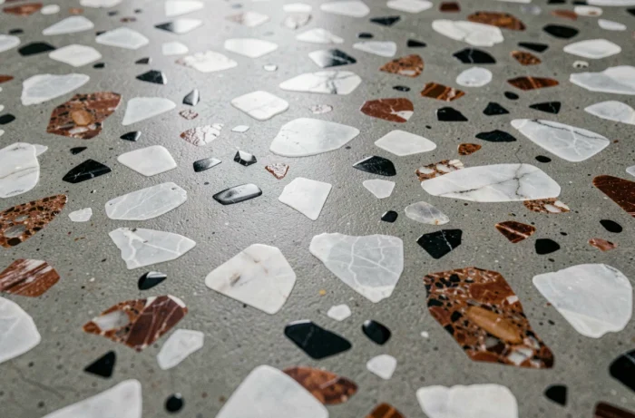 Détail de sol en terrazzo coulé sur site avec granulats sélectionnés mêlant éclats de marbre blanc, granite rouille et obsidienne noire dans une matrice ciment gris chaud.